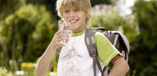 Ein Schulkind steht mit einem Glas Wasser in der Hand.