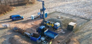 Luftaufnahme einer Baustelle. Zahlreiche Baufahrzeuge sind auf dem Geländ zu sehen.Im Zentrum des Bildes ist eine Brunnenbohrung.