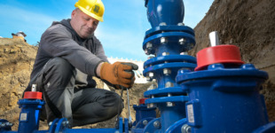 Ein Bauarbeiter in einer Baugrube. Es werden die blauen Wasserrohrleitungen erneuert.