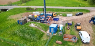 Luftaufnahme einer Baustelle in grüner Umgebung. Zahlreiche Baufahrzeuge sind auf dem Gelände.Im Zentrum des Bildes ist eine Brunnenbohrung.